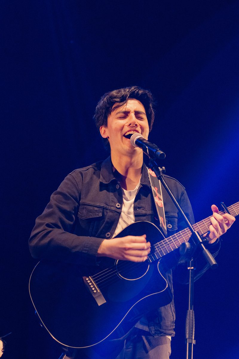 Kike de León canta con su guitarra bajo luz azul en el escenario